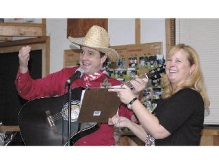 Kevin Benedict entertains the crowd at the Bonney Lake Chamber’s annual banquet. Katrina Minton holds the lyric sheet.