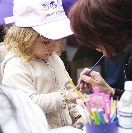 A woman paints an image on the hand of a young girl Saturday