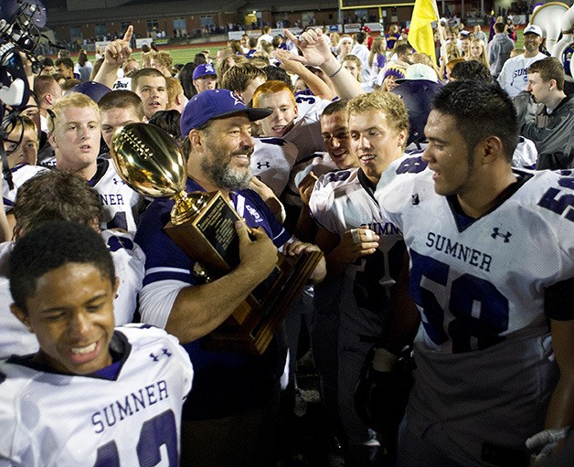 Spartan coach Keith Ross holds the Sunset Bowl trophy Friday surrounded by his team. Sumner beat Bonney Lake 49-28 at Sunset Stadium.