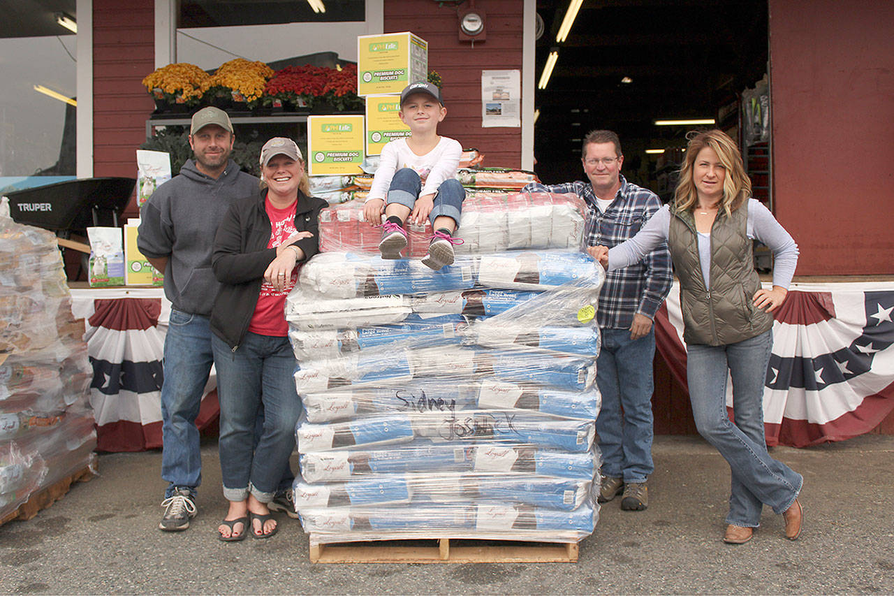 Sidney Joswick sits on top of a palette of pet food with her parents Mike and Beth to the left and Buckley Farm and Feed Supply employees Mark and Claire to the right. Photo by Ray Still