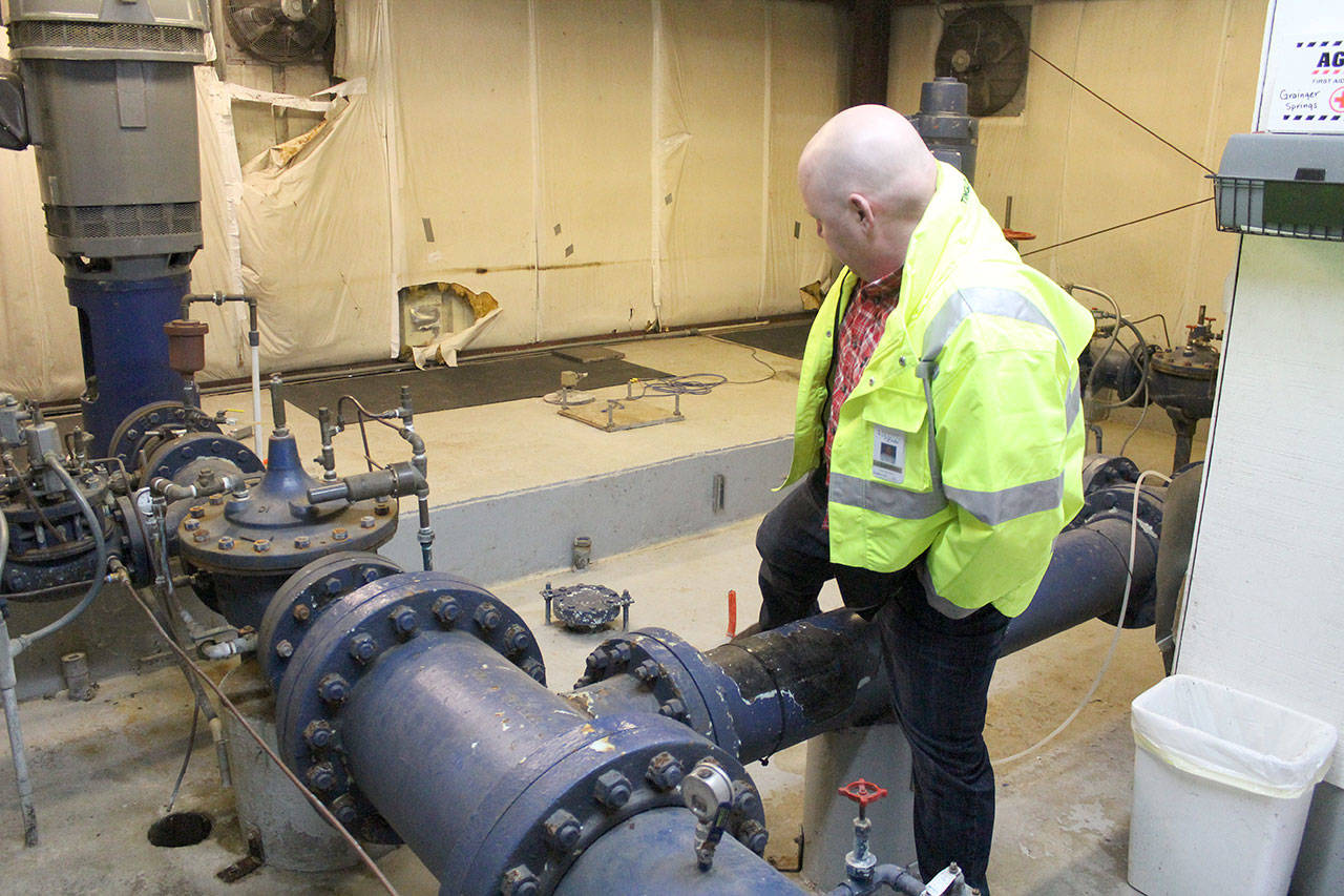 Ryan Johnstone, Bonney Lake’s superintendent of Public Works, steps over a water pipe in the Grainger Springs booster pump station, the city’s oldest water source. This small building has several issues that need to be addressed — some pumps and electrical equipment were made in the ‘70s, the building flooded three feet deep at least two decades ago and damaged the building and some equipment, pipes obstruct free movement, underground water reservoirs are slowly falling away from the building, and there are even bullet holes in one wall. Photo by Ray Still