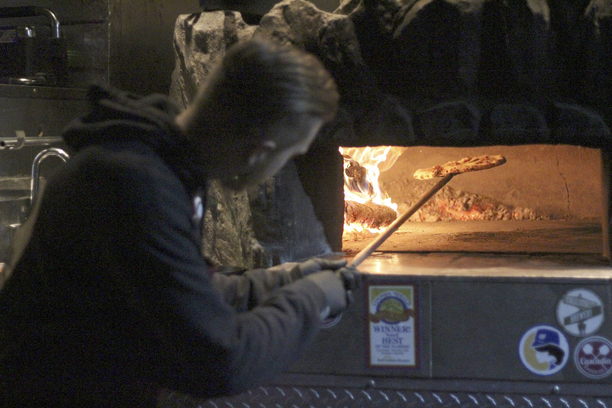 Cascadia Pizza Co. baker Stephen Hendrickson checks his pizza while waiting for business outside Headworks Brewing to pick up. Unlike many food trucks, Cascadia customers can watch everything its bakers do, since the oven is located on the outside. Photo by Ray Miller-Still