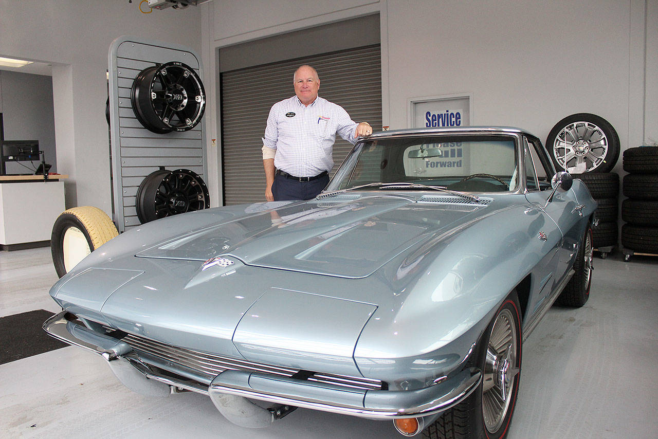 Alan Gamblin, who took over his father’s dealership in 1985, stands in his car shop next to his personal 1964 Corvette. Photo by Ray Miller-Still