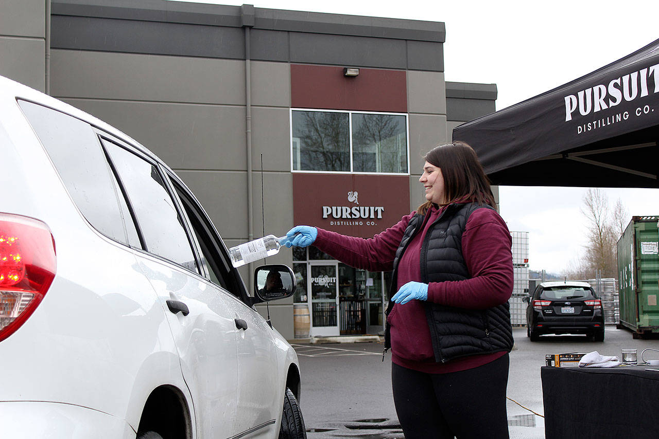 Local resident Riley Maples hands out 1-liter bottles of hand sanitizer right outside Pursuit Distillery. When its doors opened at 10 a.m. last Wednesday, the line of cars already stretched back to Battersby Avenue. Photo by Ray Miller-Still