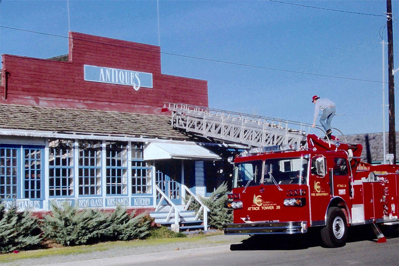Walt Olsen climbs a ladder to remove the “Dave’s Antiques” sign from Buckley Hall. The fire equipment was provided by Joe Kolisch, a former Enumclaw fire chief. Photo courtesy the Foothills Historical Society