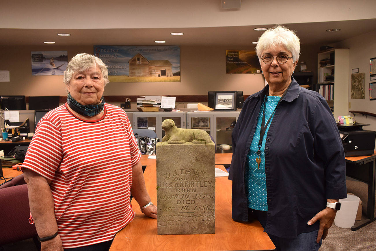 JoAnn Taylor, left, and Winona Jacobsen, right, pose for a picture at the Bonney Lake Public Works Center flanking the gravemarker of former Lake Tapps area Daisey Kirtley, who died in 1886 at the age of eight. This year, her gravemarker is being reunited with her family at the Buckley Cemetery.