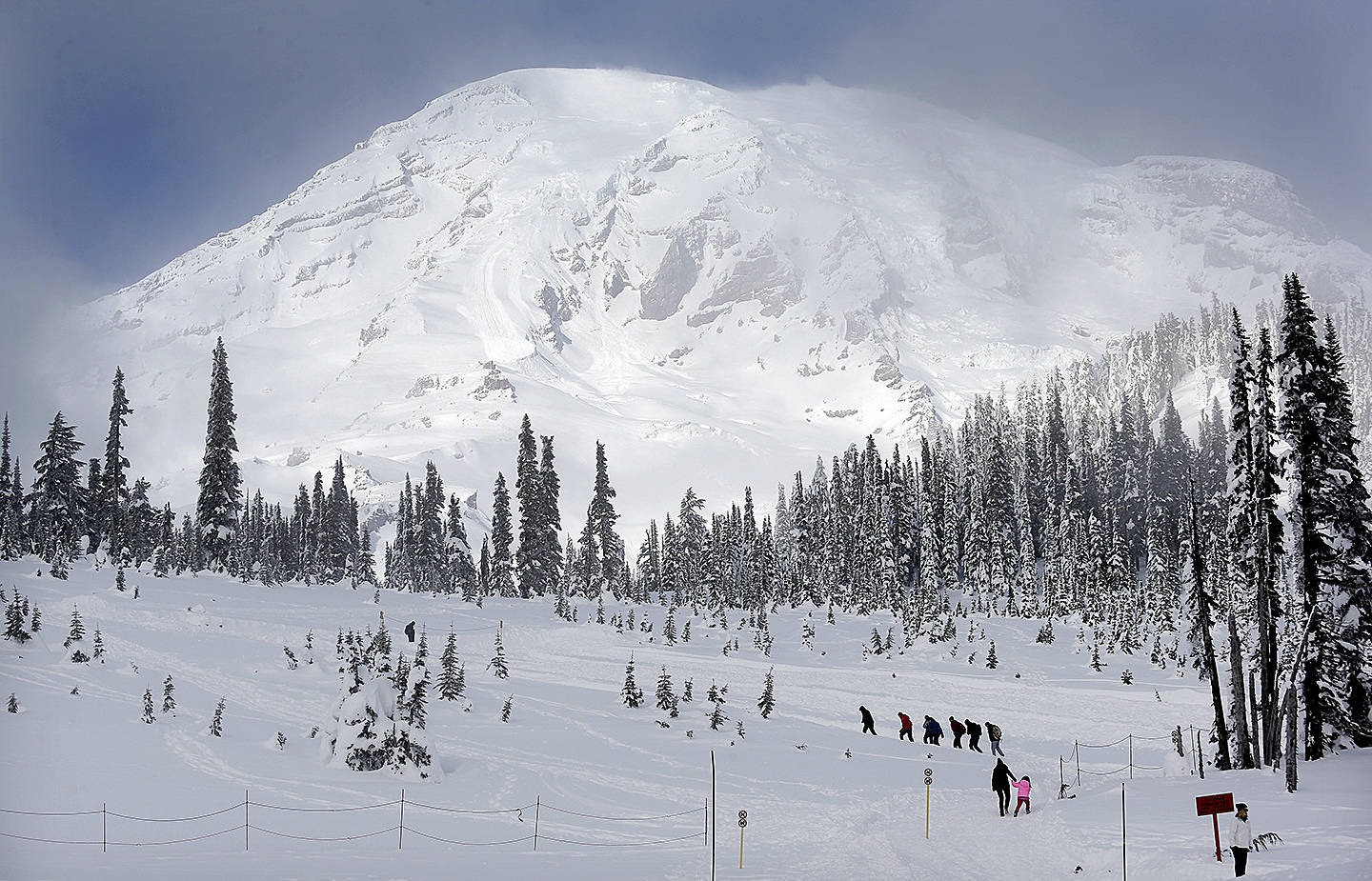 In this photo taken Friday, Dec. 16, 2016, Mount Rainier fills the sky behind as a group of snowshoers head out of the Paradise area for an outing at Mount Rainier National Park, Wash. (AP Photo/Elaine Thompson)