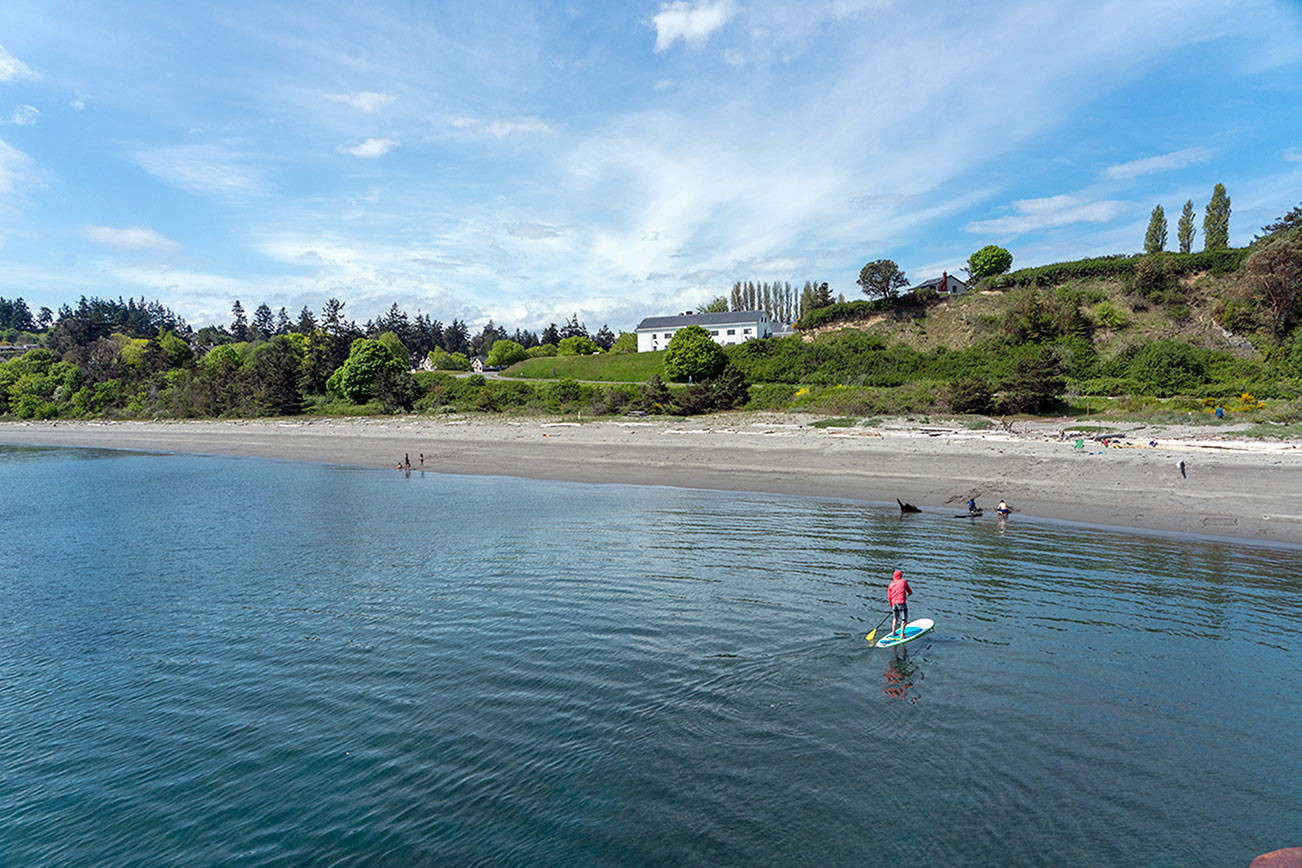 Steve Mullensky/for Peninsula Daily News Mike Kane, from Port Townsend, guides his stand up paddle board to the beach at Fort Worden State Park on Tuesday. His two sons are playing on the beach in front of him. Kimball lives close to the park but this was the first day he was able to drive to the park with his SUP.