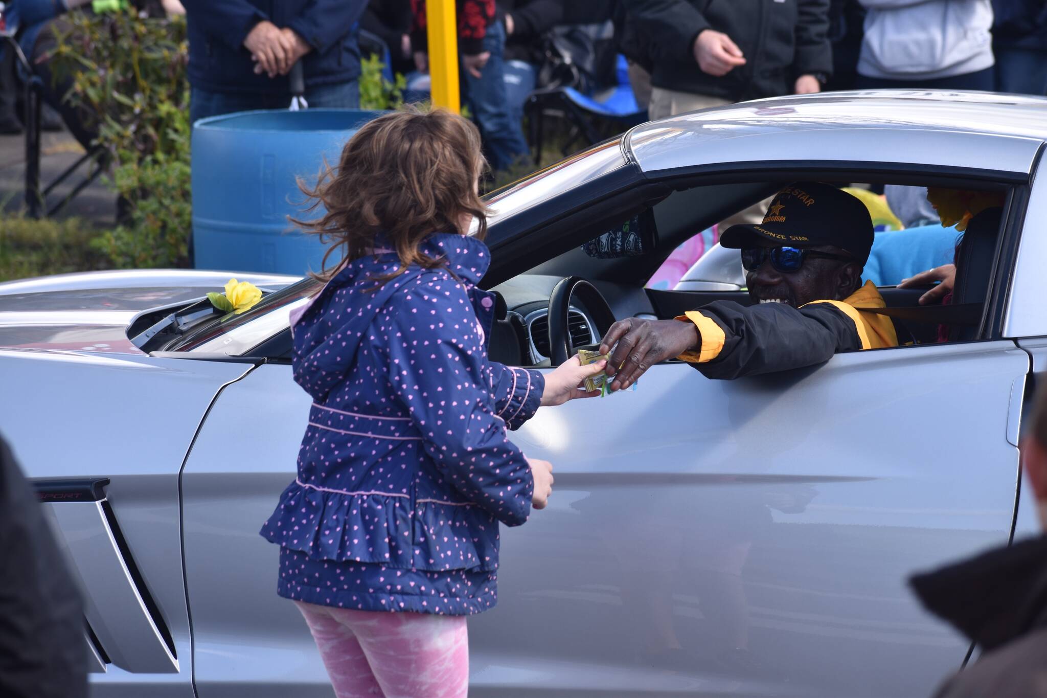 A child accepts a gift from a smiling driver in the Daffodil Parade during its run through Puyallup. Photo by Alex Bruell
