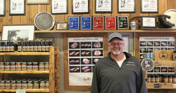 Adam Olson standing in front of Olson's Meats numerous Northwest Meat Processors Association championship awards. Adam sausages also earned the grand champion title in the national American Cured Meats Championships in 2011. Photo by Ray Miller-Still