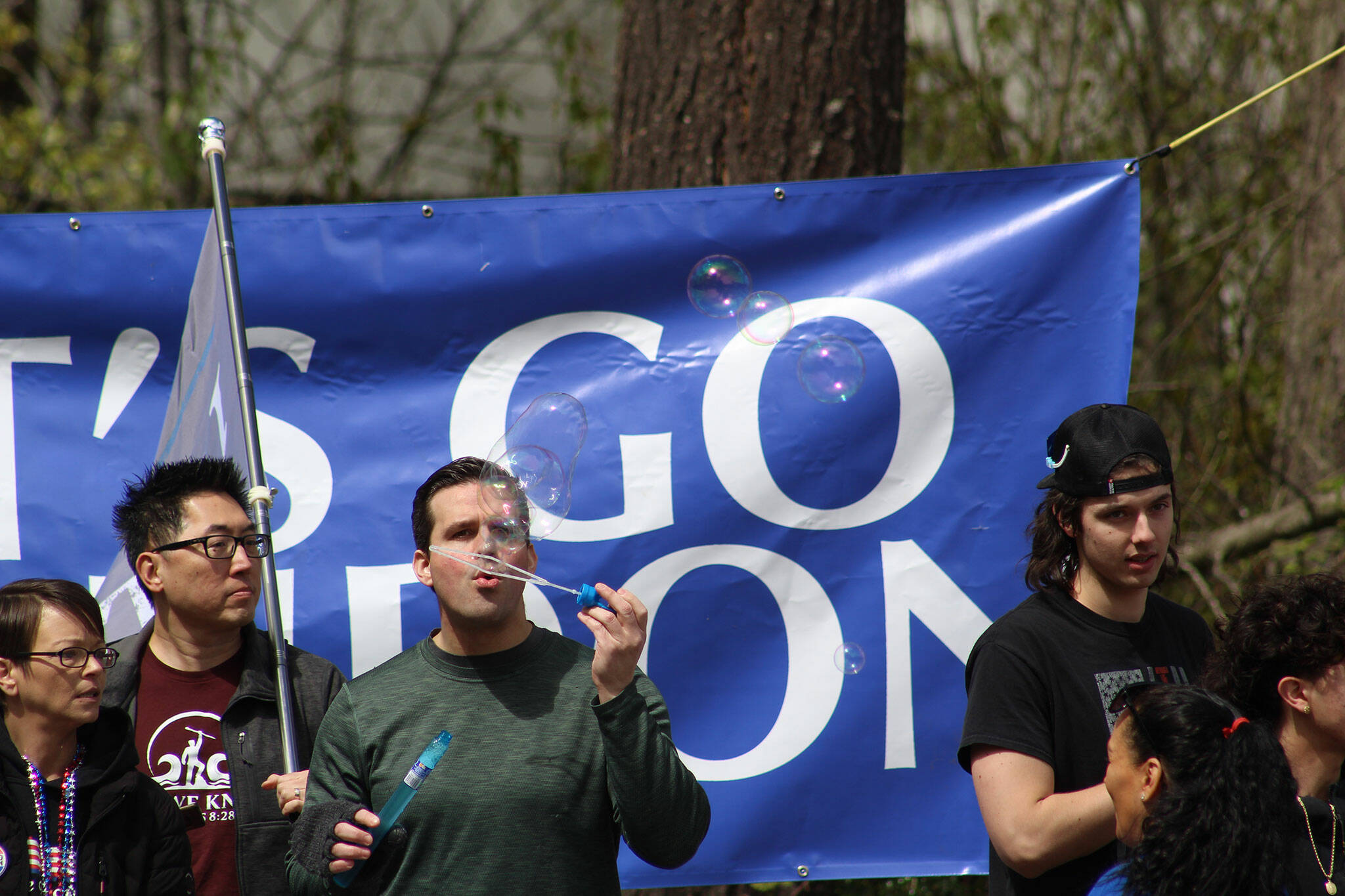 A member of the crowd blows bubbles in front of a giant “LET’S GO BRANDON” sign as the crowd awaits the arrival of President Biden. Photo by Alex Bruell/Sound Publishing