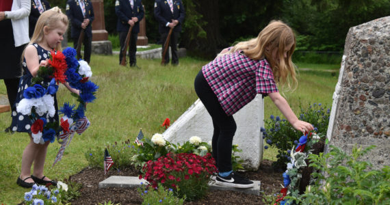 `Photo by Alex Bruell
Mila Finn (left), 4, and Aria Finn, 6, place wreaths at the base of the new Never Forget Garden.