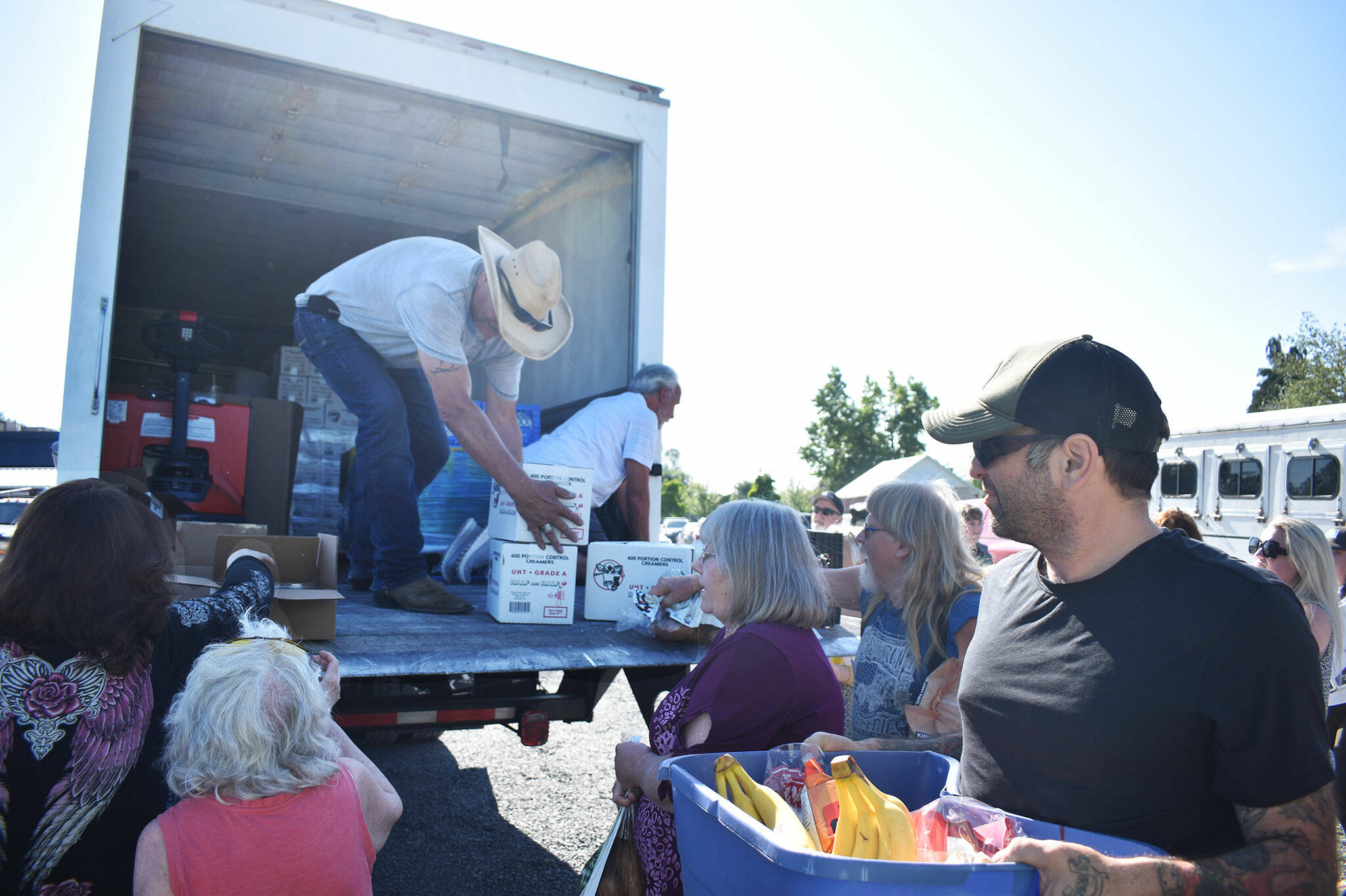 Photo by Alex Bruell
Jay Hill (cowboy hat) and Bill Petersen, warehouse supervisors at the Sumner Food Bank, unload food for families on July 13 in the parking lot of the Buckley Eagles’ hall atop their truck from the Sumner Food Bank.