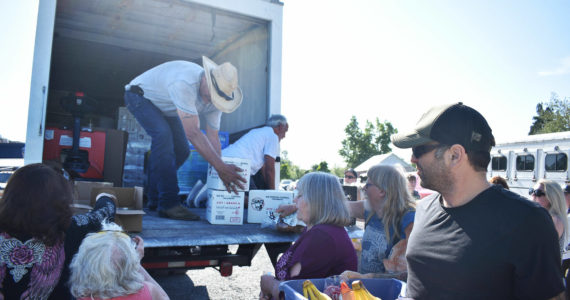 Jay Hill (cowboy hat) and Bill Petersen, warehouse supervisors at the Sumner Food Bank, unload food for families on July 13 in the parking lot of the Buckley Eagles’ hall atop their truck from the Sumner Food Bank. Photo by Alex Bruell.