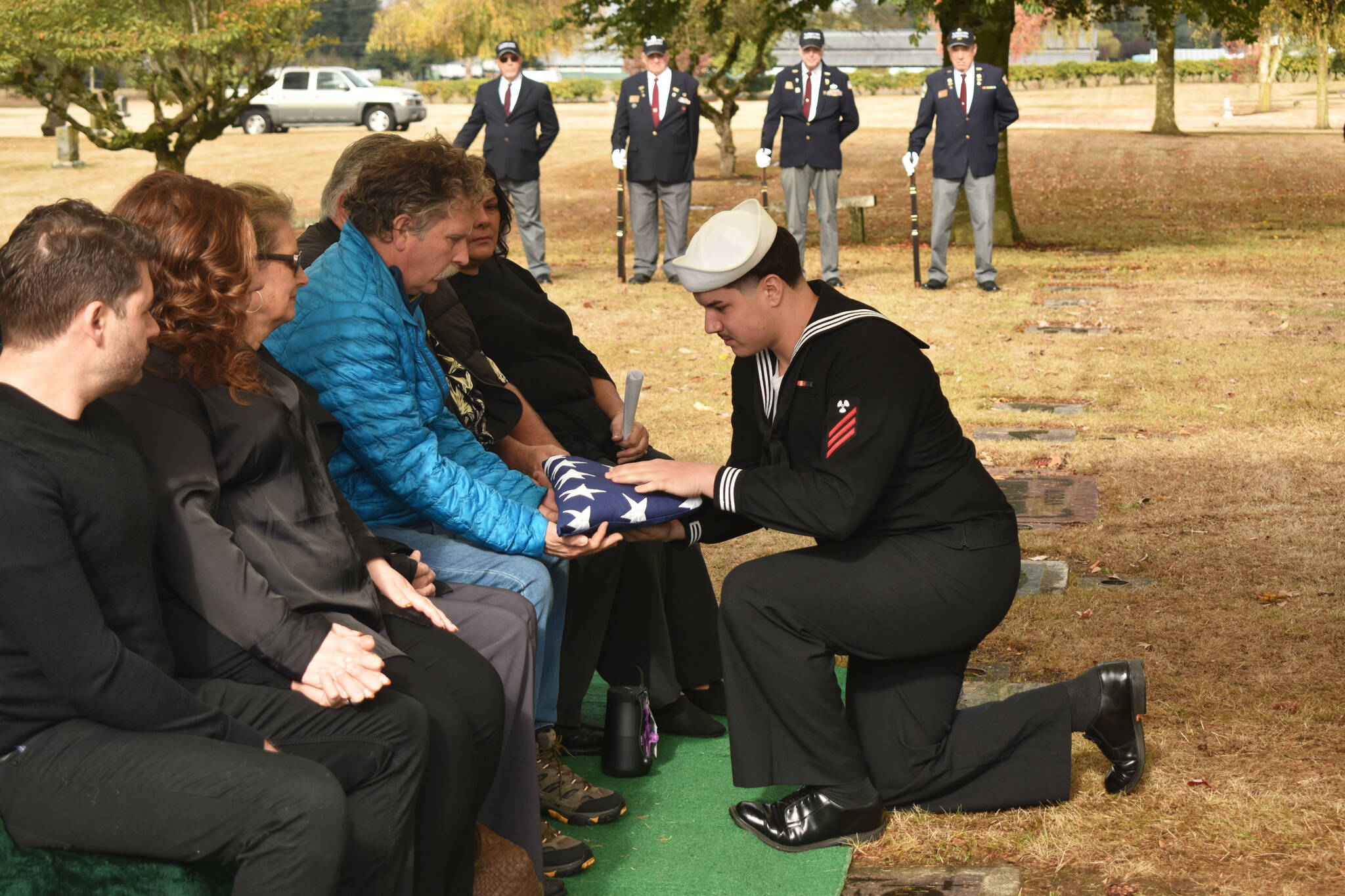 In these photos, two young men in their Naval service uniforms fold and present a United States flag to Jeff Jagosh, one of the children of the recently deceased Enumclaw couple Joseph and LaDonna Jagosh. Joe, a Korean War veteran who served on the USS Bremerton-130 during the Blockade of Wonsan, was given military honors during a ceremony with the family Friday at Enumclaw Evergreen Memorial Park, including the playing of Taps and a gun salute. VFW Honor Guard Chair Al Zarb led the local VFW Post 1949 in the ceremony. LaDonna died this June at the age of 84, and Joseph died a few weeks later at 89; the two were married for 65 years. They will be buried at the cemetery with their son Dan, who died at the age of 20.