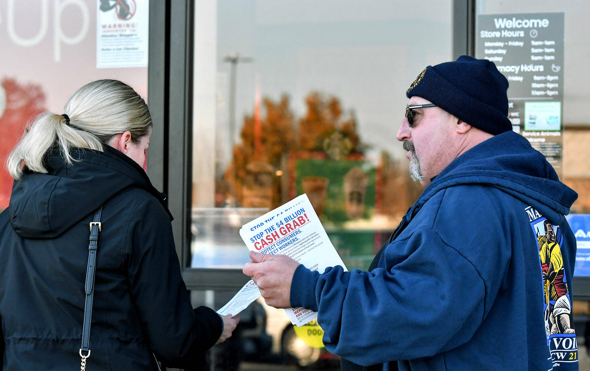 Kevin Flynn, right, a meat-cutter with the Marysville Albertsons, hands a leaflet to a shopper during an informational campaign on Wednesday. Flynn was one of less than a dozen grocery store workers handing out leaflets to shoppers about the proposed merger between Albertsons and Kroger. (Mike Henneke / The Herald)