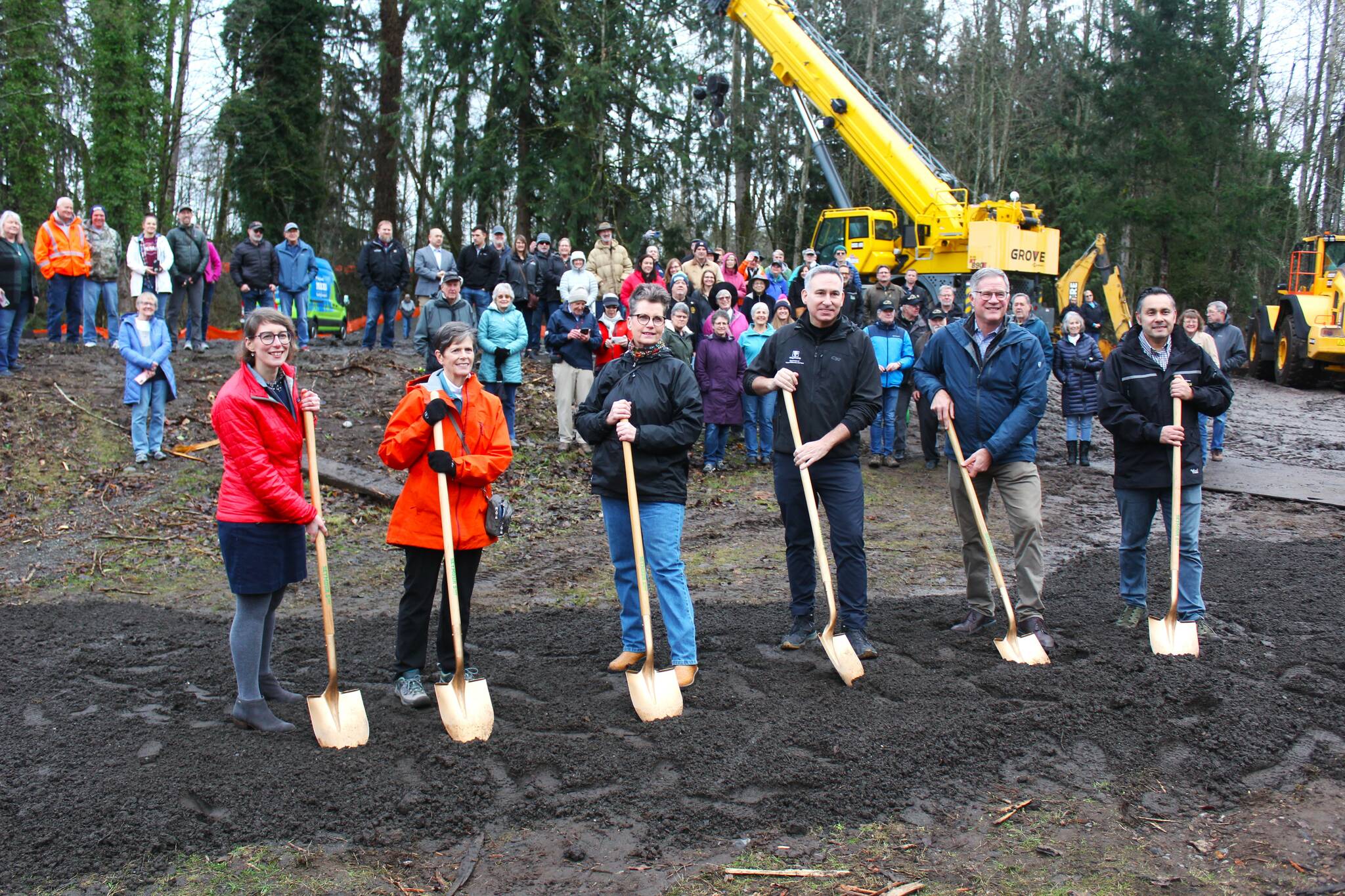 Foothills Rails to Trails Executive Director Shayla Miles, former Buckley Mayor Pat Johnson, former Enumclaw Mayor Liz Reynolds, King County Executive Dow Constantine, Pierce County Executive Bruce Dammeier, and King County Parks and Rec Director Warren Jimenez pose with their ceremonial shovels in front of the crowd gathered at the groundbreaking. Photo by Ray Miller-Still