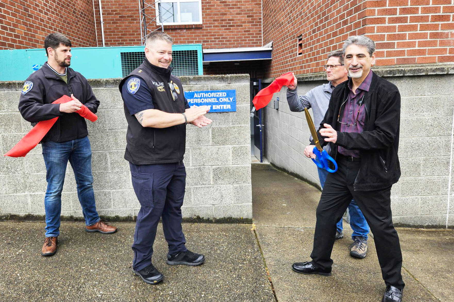 Enumclaw Police Department Corrections Officer Jessie Holman, Police Chief Tim Floyd, City Administrator Chris Searcy, and Mayor Jan Molinaro cutting the ribbon for the upgraded Enumclaw jail. You can see a video of the tour at the end of this article. Photo by Ray Miller-Still