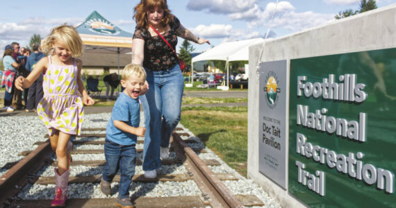 Photo by Ray Miller-Still
Douglas “Doc” Tait’s great-grandkids Welles and Brooklyn Crowther, and their aunt Brenna Tait Colo, enjoying the railroad track feature at the new Foothills Trail pavilion.
