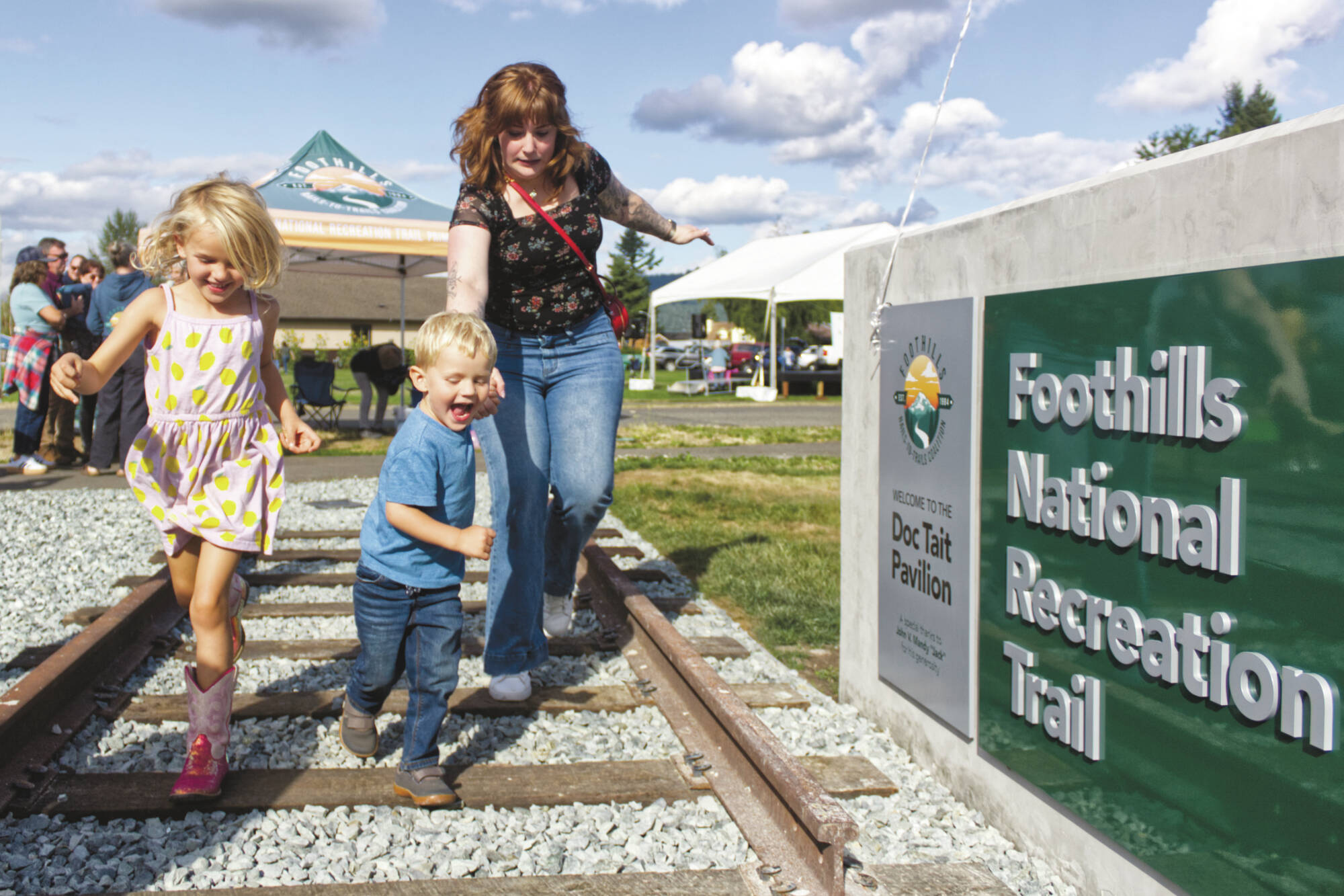 Douglas “Doc” Tait’s great-grandkids Welles and Brooklyn Crowther, and their aunt Brenna Tait Colo, enjoying the railroad track feature at the new Foothills Trail pavilion. Photo by Ray Miller-Still
