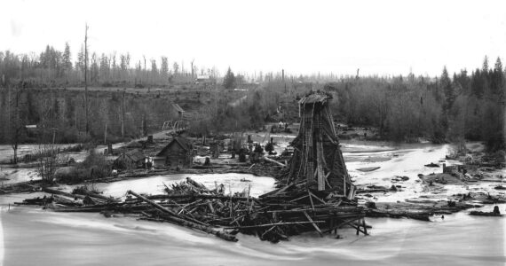 Photo by Karl Jensen / courtesy Enumclaw Plateau Historical Museum
To the left of this photo, which faces Enumclaw, is the first White River Bridge, part of the planned Naches to Yakima highway. That bridge was first built in 1897, then lost in a 1908 flood. Two houses are visible between the flooded road and the railroad trestle. Boise Creek can be faintly seen between the two bridges, where it drops 70 feet from the Enumclaw Plateau to the White River channel.
