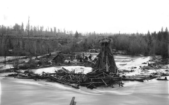 Photo by Karl Jensen / courtesy Enumclaw Plateau Historical Museum
To the left of this photo, which faces Enumclaw, is the first White River Bridge, part of the planned Naches to Yakima highway. That bridge was first built in 1897, then lost in a 1908 flood. Two houses are visible between the flooded road and the railroad trestle. Boise Creek can be faintly seen between the two bridges, where it drops 70 feet from the Enumclaw Plateau to the White River channel.