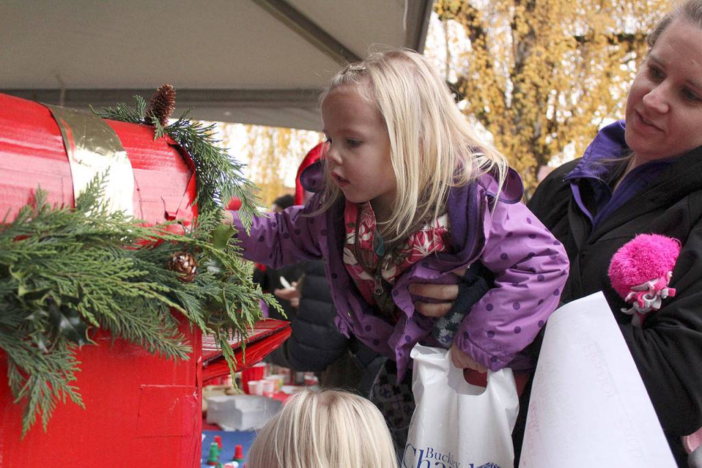 Isabelle Banks, 3, gets a boost from her mother to drop her letter to Santa into his mailbox at last years tree lighting in Buckley. Photo by Ray Miller-Still