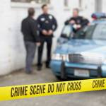 Male police officers standing behind Do Not Cross tape