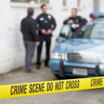 Male police officers standing behind Do Not Cross tape