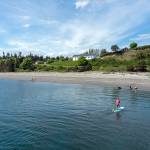 Steve Mullensky/for Peninsula Daily News Mike Kane, from Port Townsend, guides his stand up paddle board to the beach at Fort Worden State Park on Tuesday. His two sons are playing on the beach in front of him. Kimball lives close to the park but this was the first day he was able to drive to the park with his SUP.