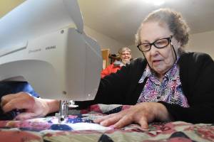 At her Enumclaw home on Feb. 22, Naomi Allen works on her latest quilt to be delivered to seniors in town. Her friend Janine Carpenter, in the background, talks to Allen regularly and helps deliver the quilts to the seniors who need them. Photo by Alex Bruell