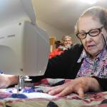 At her Enumclaw home on Feb. 22, Naomi Allen works on her latest quilt to be delivered to seniors in town. Her friend Janine Carpenter, in the background, talks to Allen regularly and helps deliver the quilts to the seniors who need them. Photo by Alex Bruell