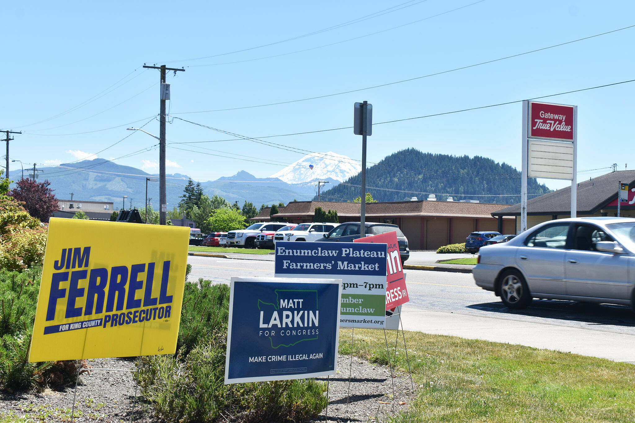 Political campaign signs, as well as a sign for the Enumclaw Plateau Farmers Market, are posted along Highway 410 in Enumclaw on a hot July afternoon. Mount Rainier appears in the background. Photo by Alex Bruell.