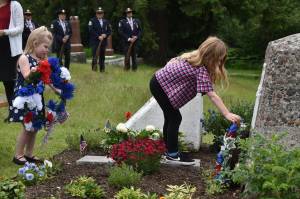 `Photo by Alex Bruell
Mila Finn (left), 4, and Aria Finn, 6, place wreaths at the base of the new Never Forget Garden.