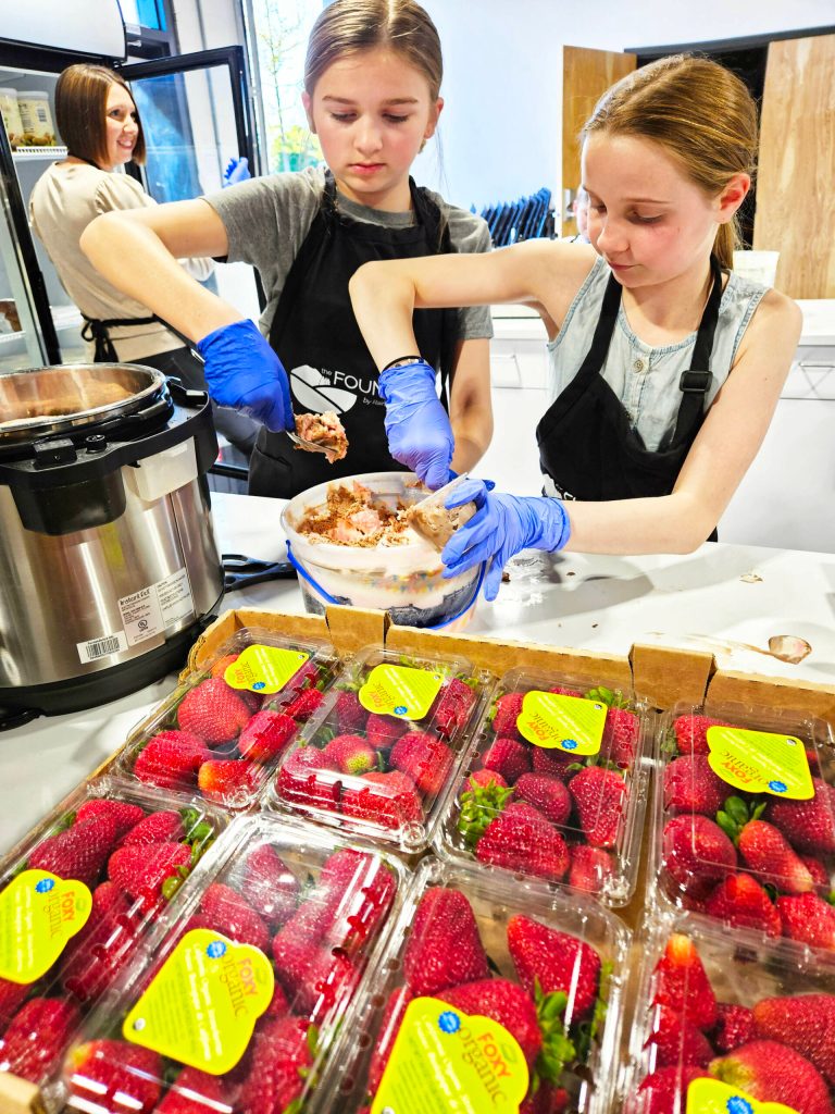 Molly Dacey and Addy Wooldridge scoop some Neapolitan ice cream into small bowls for people attending the Full Bellies free meal event on Thursdays. Photo by Ray Miller-Still