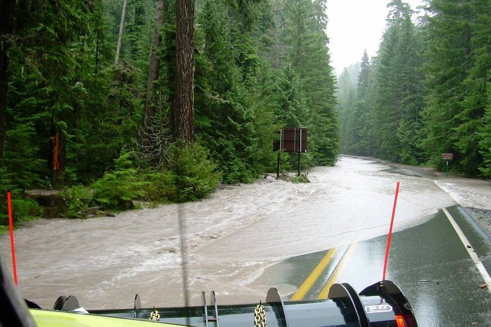 Water flows across SR 410 as machinery from the Department of Transportation works to clear water off road during a 2006 flood. Photo courtesy National Park Service