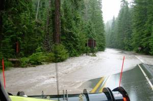 Water flows across SR 410 as machinery from the Department of Transportation works to clear water off road during a 2006 flood. Photo courtesy National Park Service